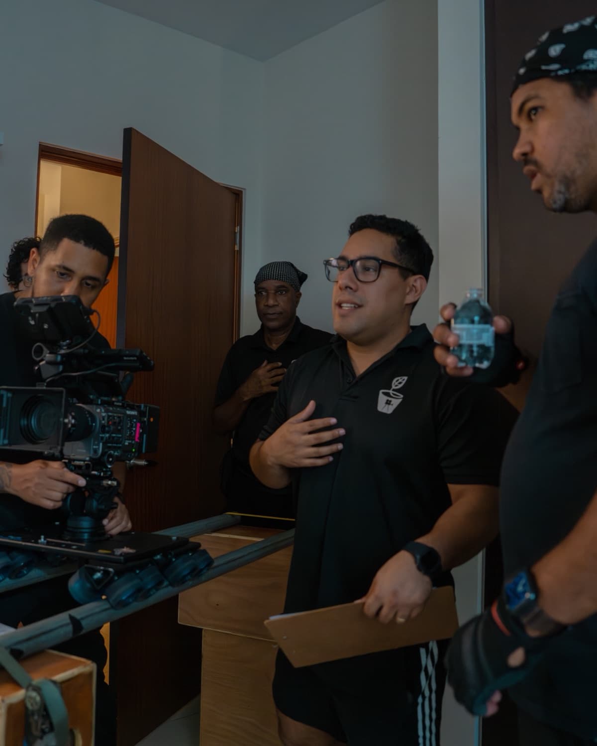 Andrés López dirigiendo a su equipo en un set interior, junto a un camarógrafo en dolly, luces y claqueta
